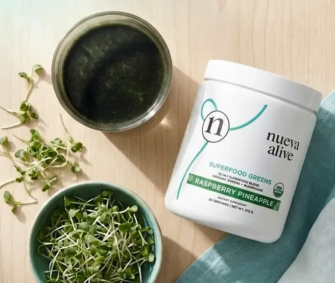 A Nueva greens powder on a kitchen counter beside fresh greens